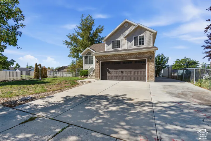 Two-story exterior featuring a brick and horizontal siding facade, an attached two-car garage, a concrete driveway, and surrounding chain-link fencing