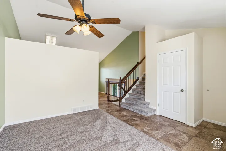 Vaulted ceilings featuring a central paddle fan, staircase with wood-finished handrail, and ceramic tile flooring