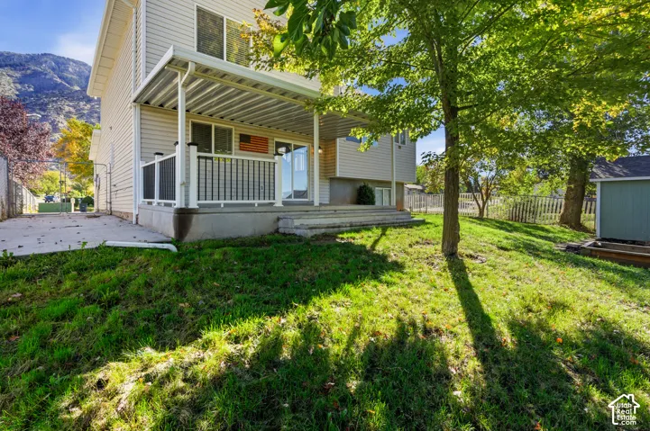 Rear exterior featuring a covered patio, metal railing, concrete hardscaping, and a mountain backdrop