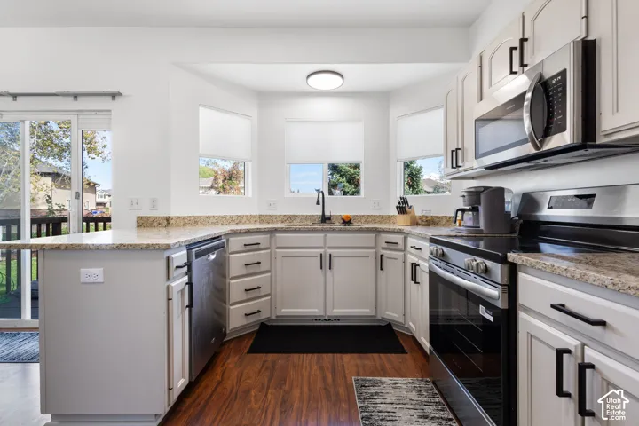 Kitchen featuring light-toned cabinetry, stone countertops, stainless steel appliances, wood-finish flooring, and a bay window