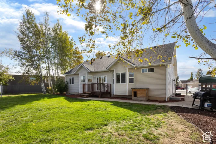 Exterior rear elevation featuring light-toned vinyl siding, a multi-gabled roofline, an elevated wooden deck, and a spacious lawn with mature trees