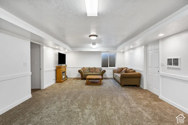 Neutral-toned interior space featuring carpeting, white wainscoting, recessed ceiling lighting, and a window with a security grate