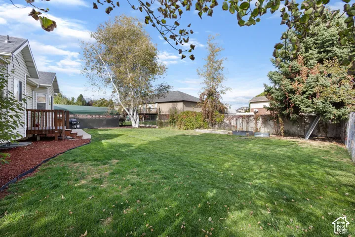 Backyard featuring a grass lawn, wood deck, wood-chip ground cover, and perimeter fencing