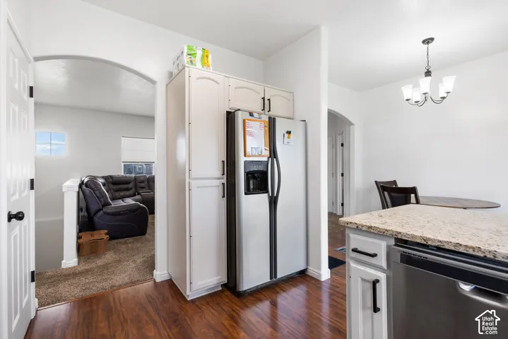 Kitchen featuring wood-finish flooring, white cabinetry with matte black hardware, stainless steel refrigerator, stone-composite countertop, and multi-light chandelier