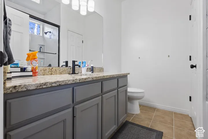 Bathroom vanity featuring grey shaker-style cabinetry, a stone countertop, matte black faucet, full-width mirror, and multi-bulb overhead lighting
