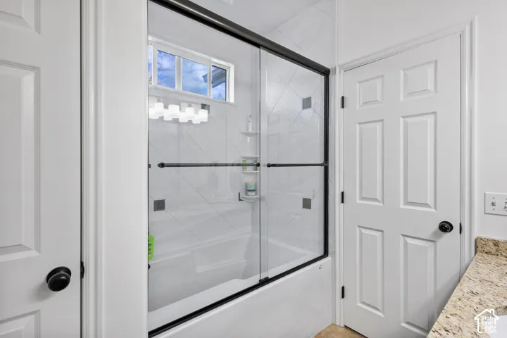 Bathtub and shower combination featuring a glass enclosure with a dark finish frame, white diagonal-set tile surround, integrated shelving, and a transom window