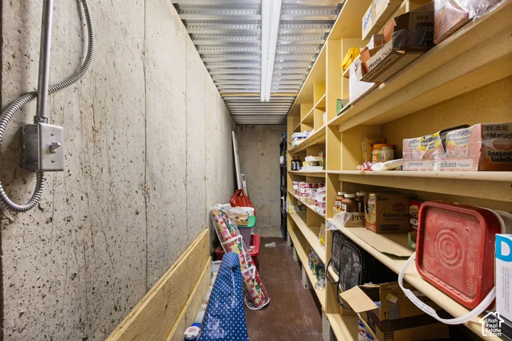 Storage area featuring built-in floor-to-ceiling wooden shelving, exposed concrete walls, and corrugated metal ceiling paneling