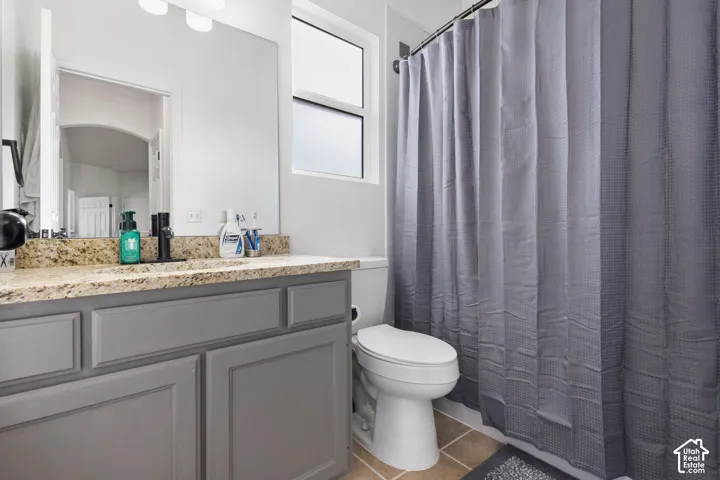 Bathroom featuring a grey-finished vanity cabinet, stone-finish countertop, undermount sink with matte black faucet, wall-to-wall mirror, and tile flooring