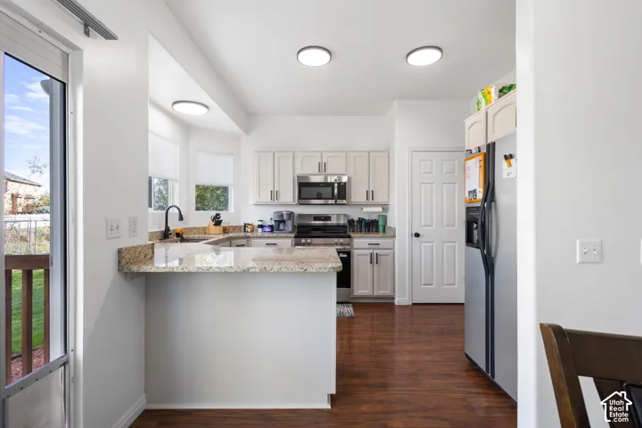 Kitchen featuring a stone-surfaced peninsula, wood-finish flooring, light-toned cabinetry, stainless steel appliances, and a single-basin sink with a matte black faucet