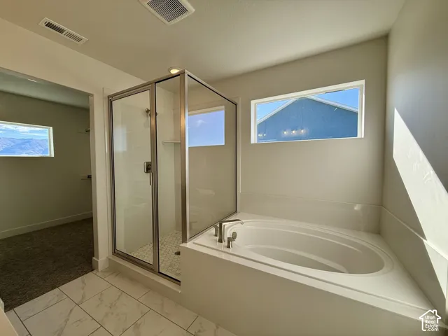 Soaking tub with a deck-mounted faucet, walk-in glass-enclosed shower, tile flooring, and rectangular windows