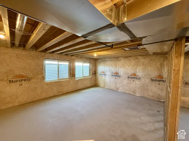 Unfinished lower level featuring exposed wood joist ceilings, concrete flooring, two sliding windows with window wells, and insulated wall paneling