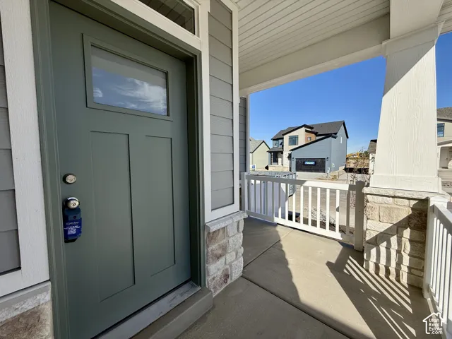 Covered front porch featuring a concrete floor, stone masonry accents, a white railing, and a paneled entry door with a transom window