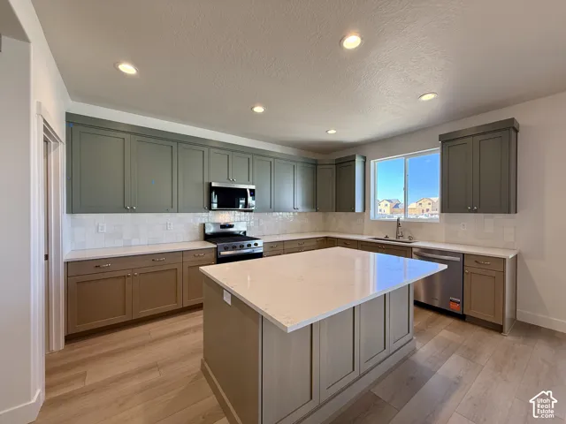 Kitchen featuring a central island with a quartz countertop, two-tone cabinetry, stainless steel appliances, and wood-finish flooring
