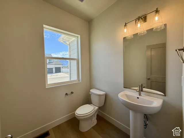 Pedestal sink with single-handle faucet, frameless wall-mounted mirror, three-light glass fixture, and wood-finish flooring