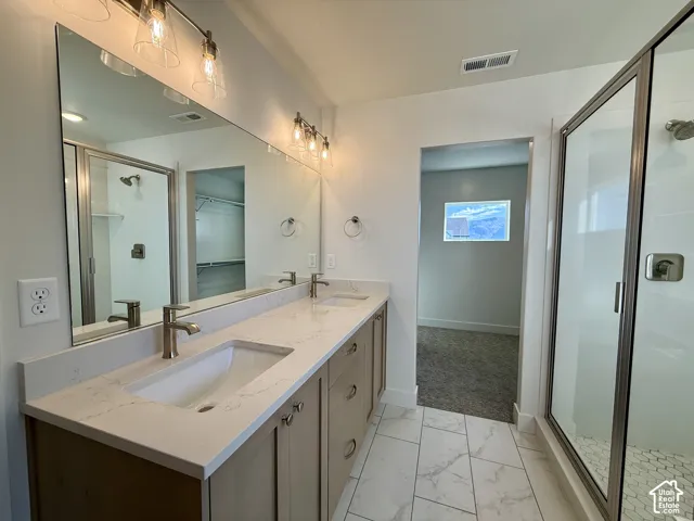 Dual-sink vanity with light-tone cabinetry and stone-composite countertops, accompanied by a glass-enclosed shower with tiled flooring and dual wall-mounted light fixtures