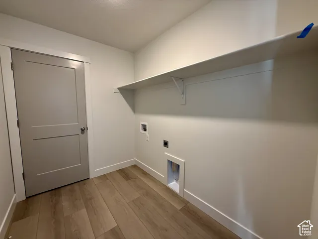 Utility area featuring wood-finish flooring, a neutral-toned shaker-style door, an extended overhead wall shelf, and dedicated water and electrical hookups