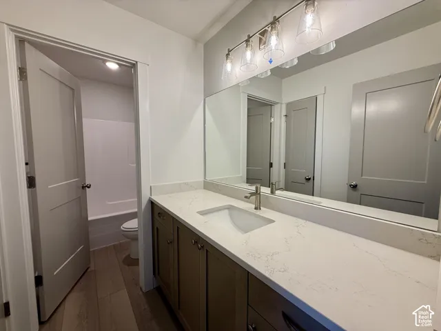 Bathroom vanity featuring a light-toned countertop with an integrated basin, wood-finish cabinetry, a large wall-mounted mirror, and a multi-light fixture