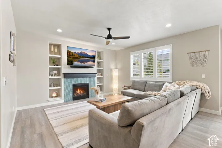 Living area featuring wood-finish flooring, recessed lighting, built-in shelving, a fireplace with a decorative tile surround, and plantation shutters