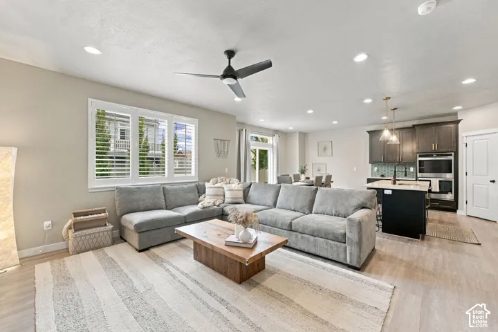 Open-concept area featuring wood-finish flooring, recessed lighting, a modern ceiling fan, plantation shutters, and a kitchen with dark cabinetry and a central island