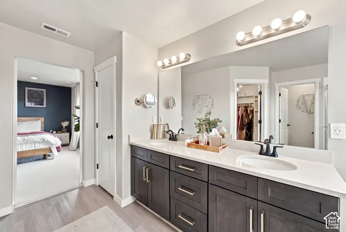 Double vanity featuring dark-toned cabinetry, light-colored stone-finish countertops, undermount sinks, matte black widespread faucets, and wall-mounted light fixtures