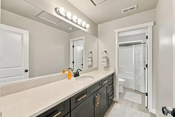 Bathroom featuring a dark-toned vanity with light-colored solid surface countertops, an expansive wall-to-wall vanity mirror, five-bulb integrated vanity lighting, and a tub-shower combination