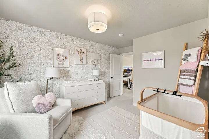 Bedroom featuring floral wallpaper accent wall, neutral carpeting, and a flush-mount drum shade light fixture