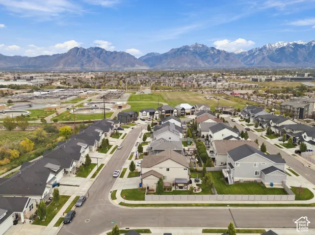 Aerial perspective of a residential community featuring multi-story dwellings, paved roadways, fenced perimeters, and a prominent mountain range backdrop