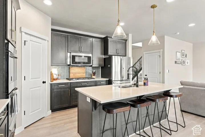 Kitchen featuring dark-stained cabinetry, central island with light-toned countertop, stainless steel appliances, and patterned tile backsplash, illuminated by dual pendant light fixtures