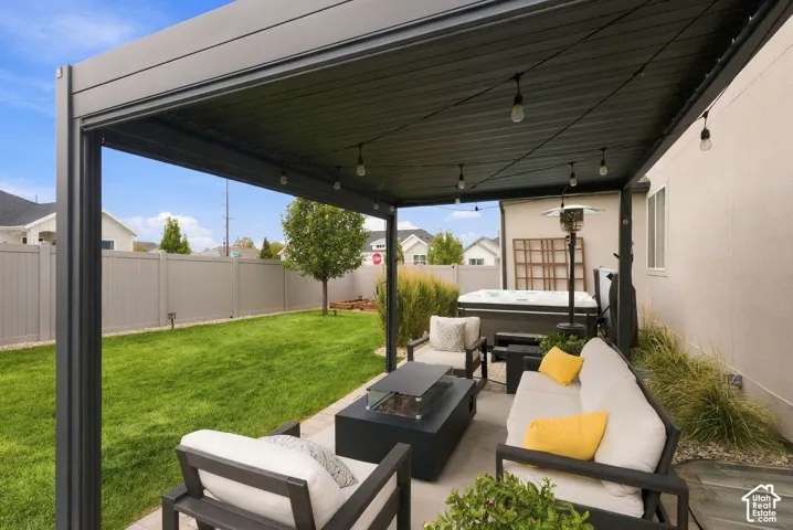 Covered patio area featuring a metal pergola, string lighting, concrete flooring, and a privacy fence