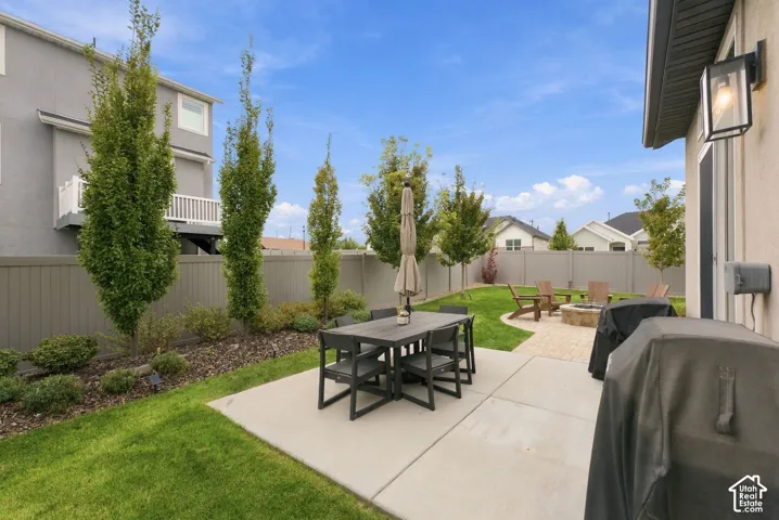 Rear yard featuring a concrete patio, a stone fire pit, a manicured lawn, perimeter fencing, and mature columnar trees