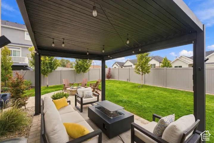 Covered patio featuring a solid-roof pergola, integrated string lighting, and paver hardscaping, complemented by a fenced backyard with a grass lawn