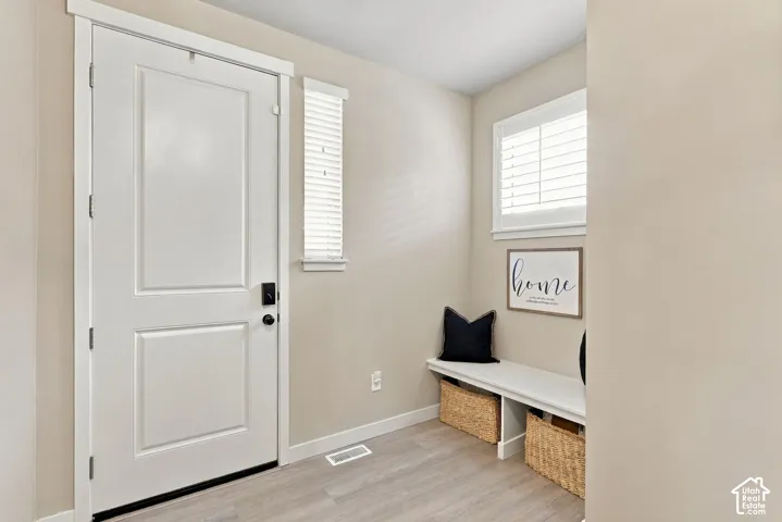 Entryway featuring a white paneled door, wood-finish flooring, built-in bench seating, and windows with white plantation shutters
