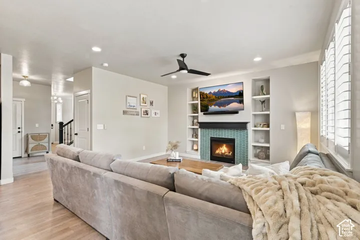 Living area featuring a floor-to-ceiling tiled fireplace surround, custom built-in shelving, wood-finish flooring, recessed lighting, and a modern ceiling fan