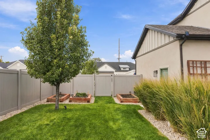 Fenced backyard featuring three raised planter beds, mature landscaping, manicured lawn, and decorative gravel pathways