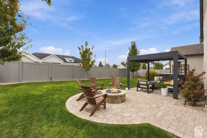 Backyard featuring a paver patio with a built-in stone fire pit, a covered metal pergola, and perimeter vinyl fencing