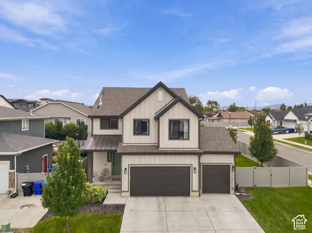 Two-story exterior featuring vertical siding, metal roofing accents, a concrete driveway, a three-car garage, and fenced perimeter