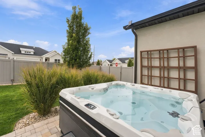 Outdoor hot tub set on a paver patio, featuring a wooden wall-mounted trellis, manicured lawn, and privacy fencing