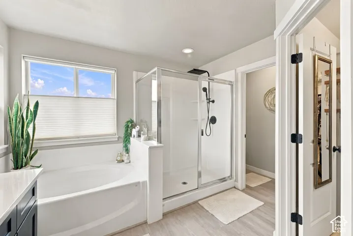 Bathroom featuring a deep soaking tub, separate glass-enclosed shower with a matte black rainfall showerhead, recessed lighting, and wood-finish flooring