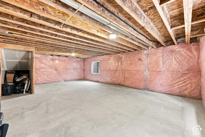 Unfinished lower level featuring exposed wood joist ceilings, poured concrete flooring, pink insulation-wrapped walls, and a single egress window