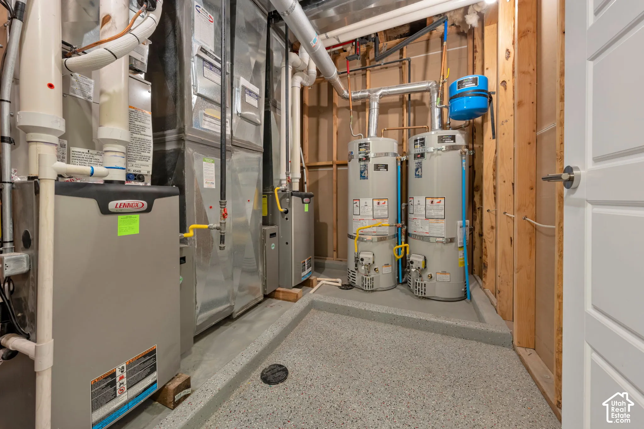 Utility room featuring dual water heaters, a forced-air furnace system, exposed structural framing, and a textured epoxy flooring surface
