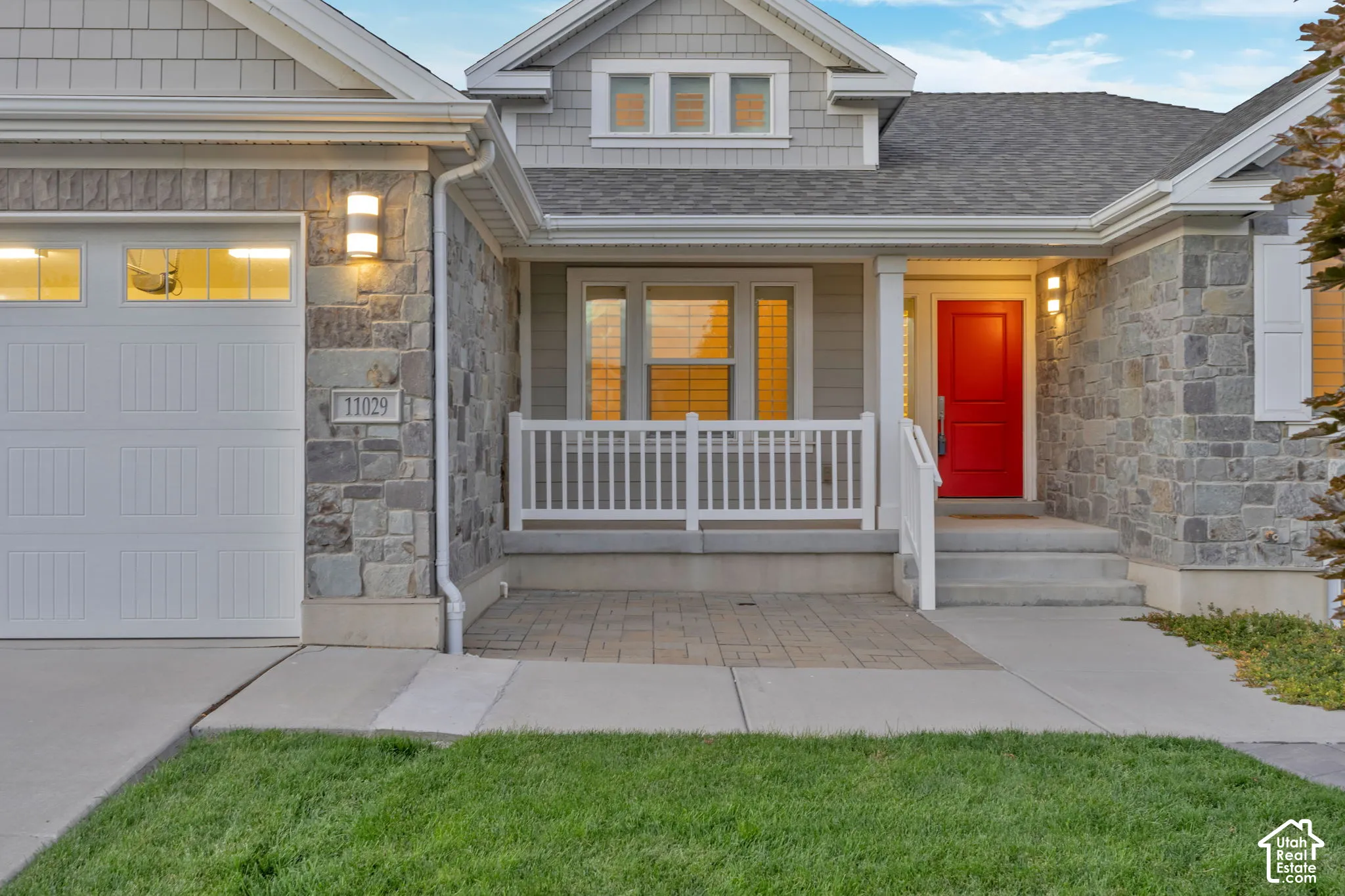 Exterior facade featuring stone veneer siding, cedar shake accents, a covered front porch with white railing, and a vibrant red entry door
