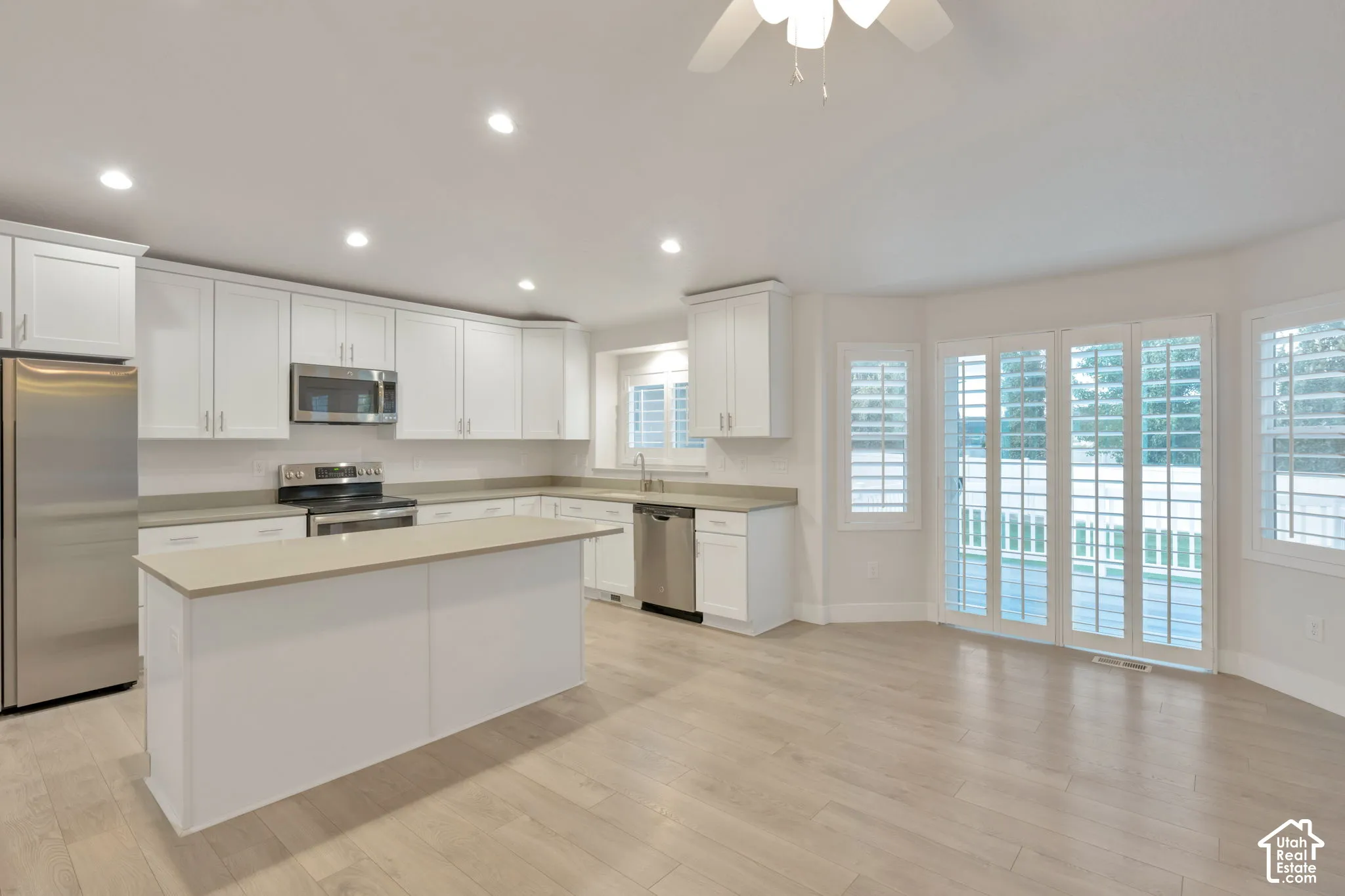 Kitchen featuring white cabinetry, an island with countertop seating, stainless steel appliances, wood-finish flooring, and shutter-style window coverings