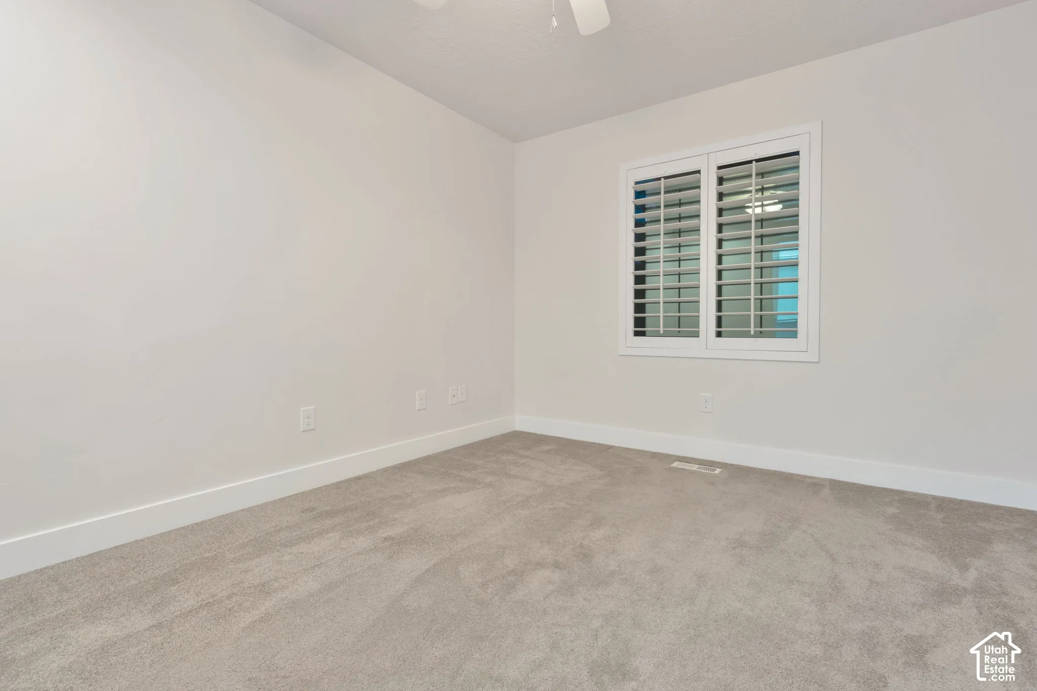 Room featuring neutral-toned carpeting, crisp wall finishes, plantation shutters, and an overhead ceiling fan
