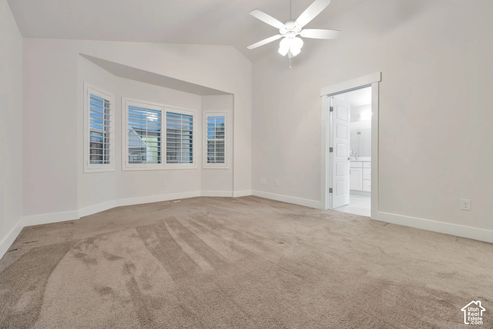 Room featuring vaulted ceilings, a bay window with plantation shutters, carpeted flooring, and a ceiling fan