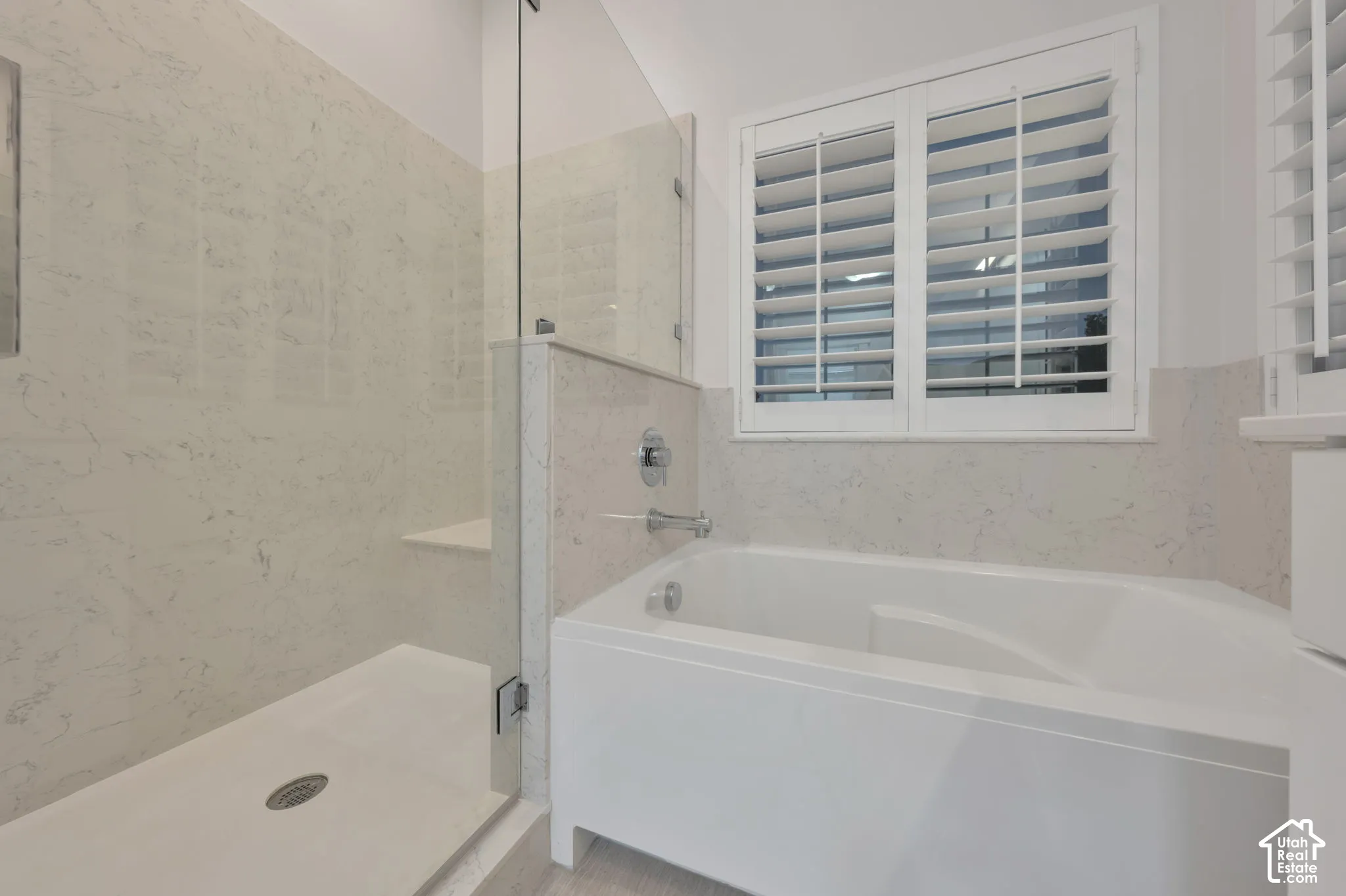 Walk-in shower with stone-surround wall tiling, built-in bench seat, and glass partition, alongside a deep soaking tub with chrome fixtures and plantation shutters