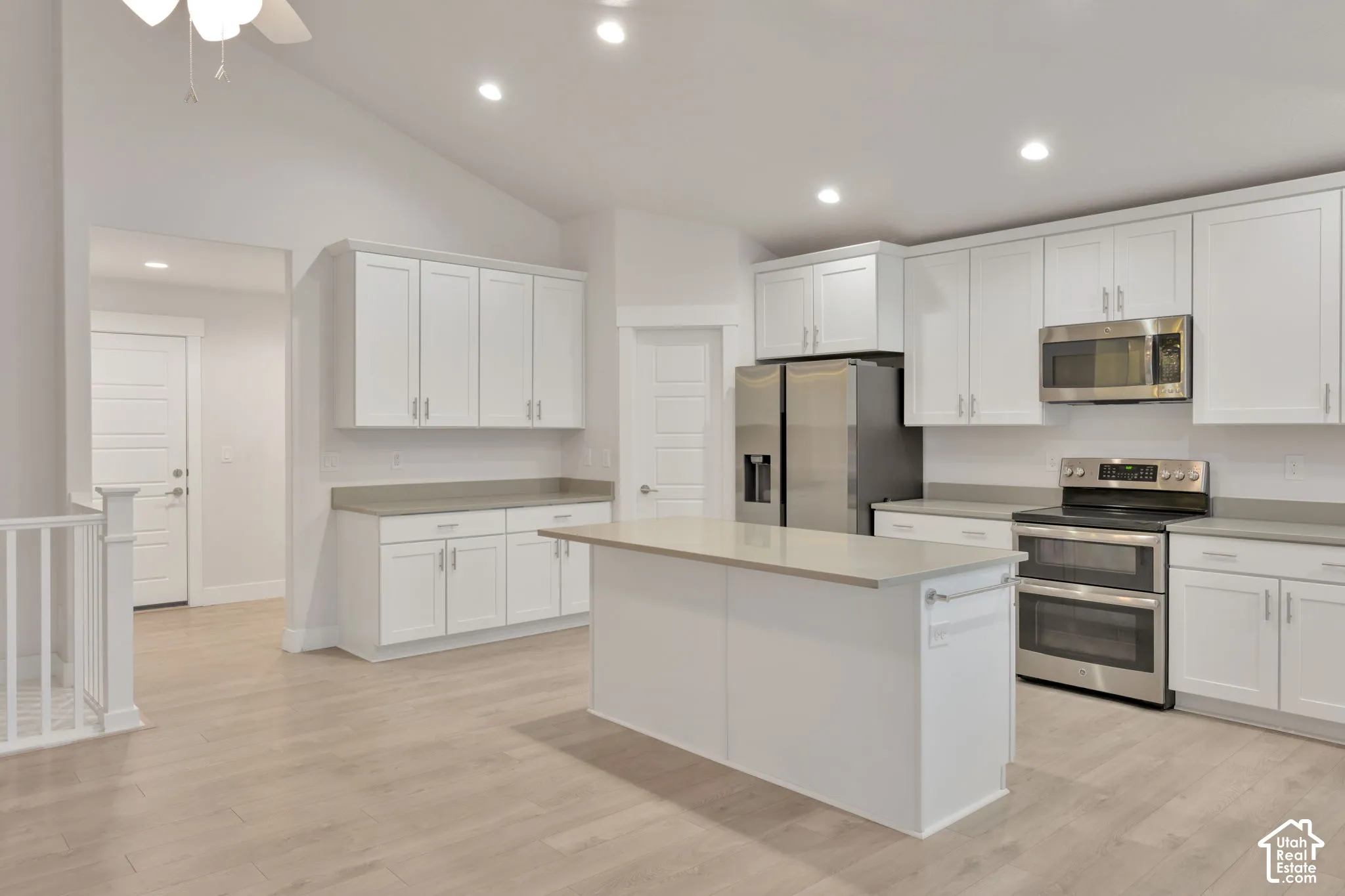 Kitchen featuring a vaulted ceiling, white shaker-style cabinetry, neutral-toned countertops, a center island, and wood-finish flooring