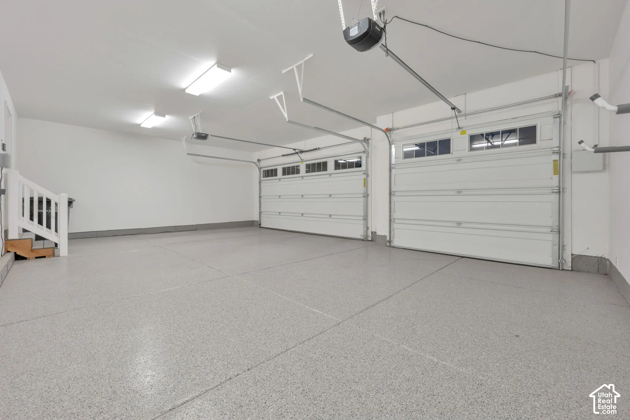 Three-car garage featuring epoxy-coated flooring, white paneled sectional doors with windows, bright overhead lighting, and white finished walls