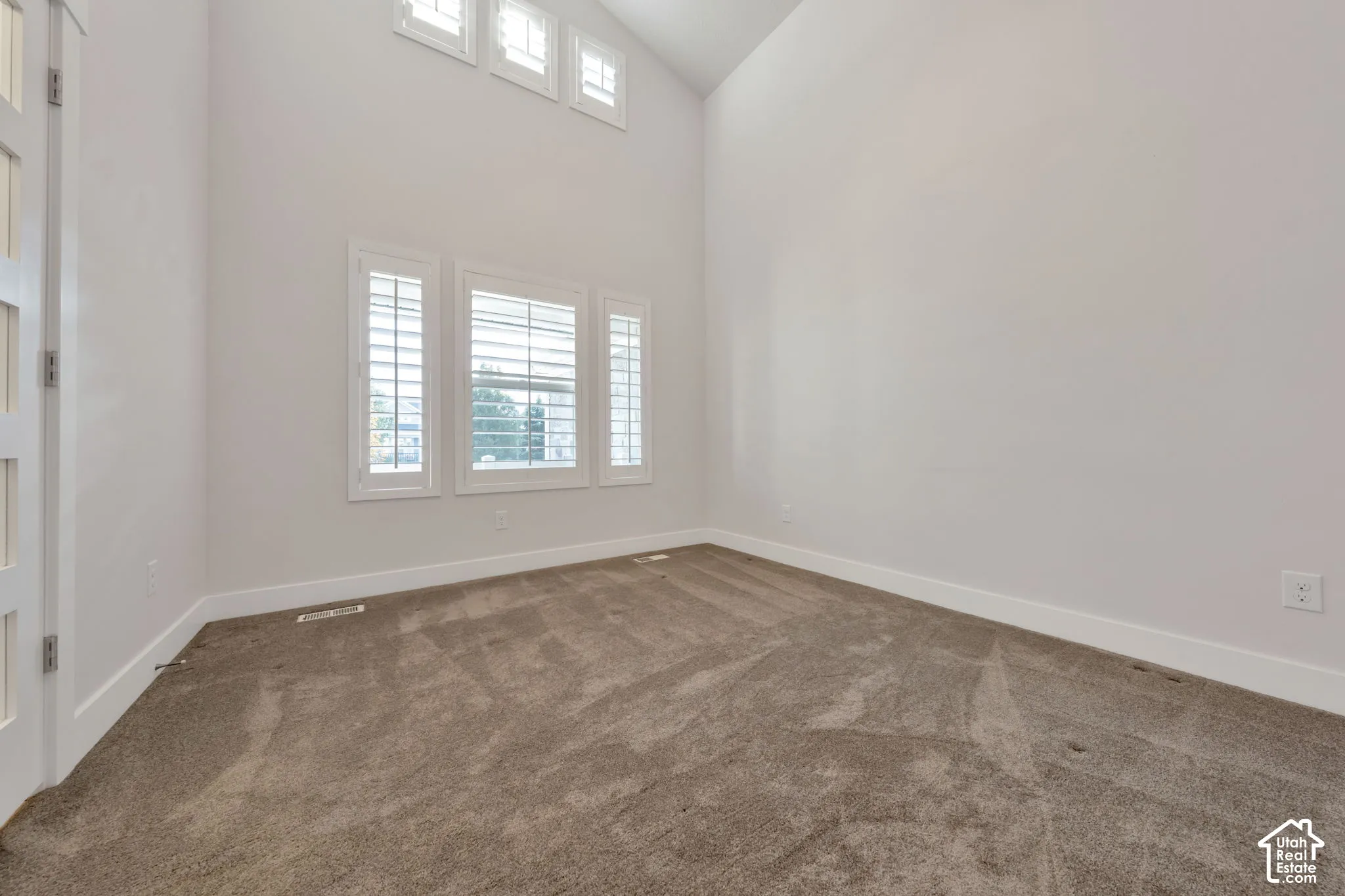 Vaulted ceilings featuring high-reach windows, wall-to-wall carpeting, and adjustable plantation shutters