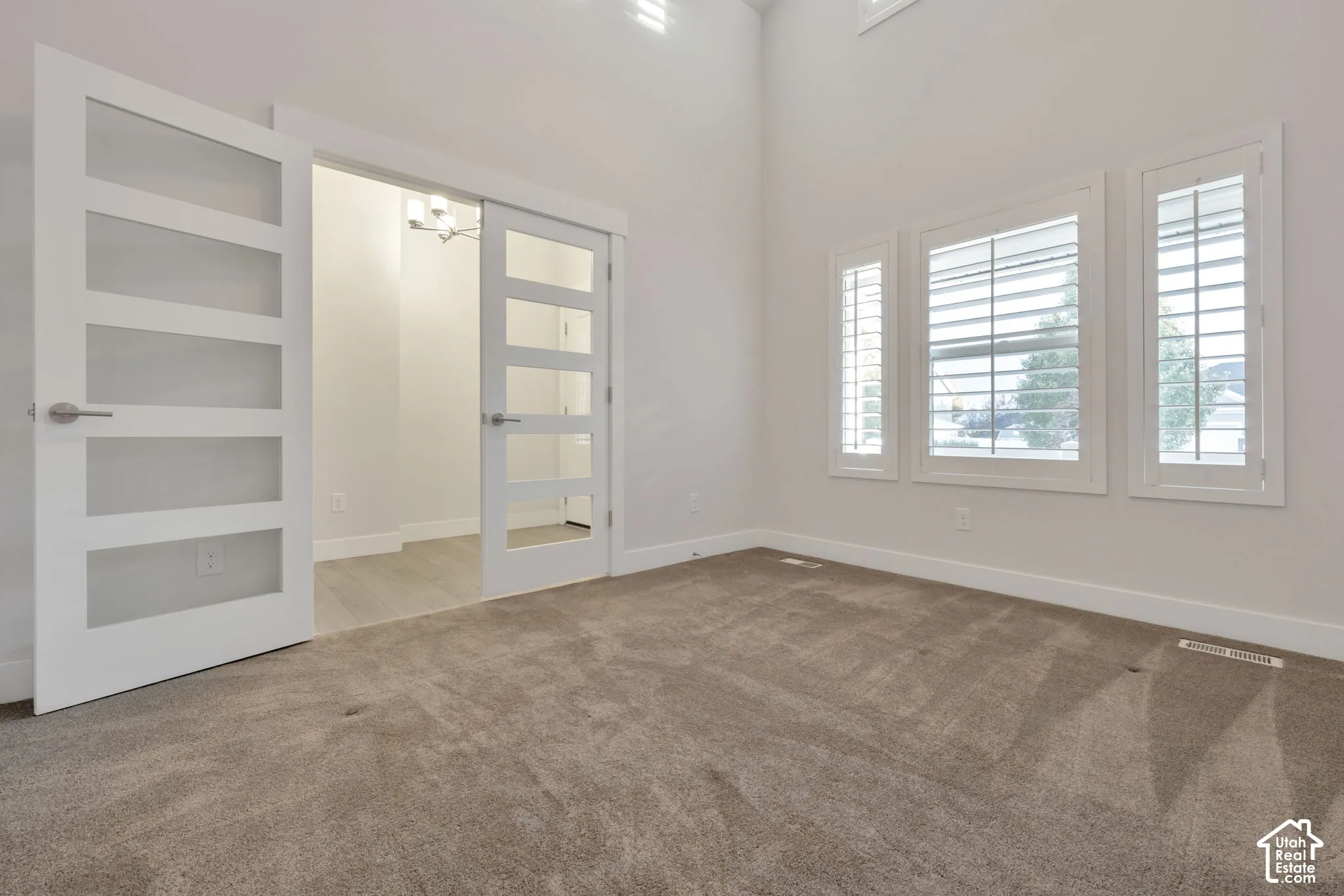 Flex-room featuring high ceilings, white paneled French doors with glass inserts, and windows fitted with plantation shutters