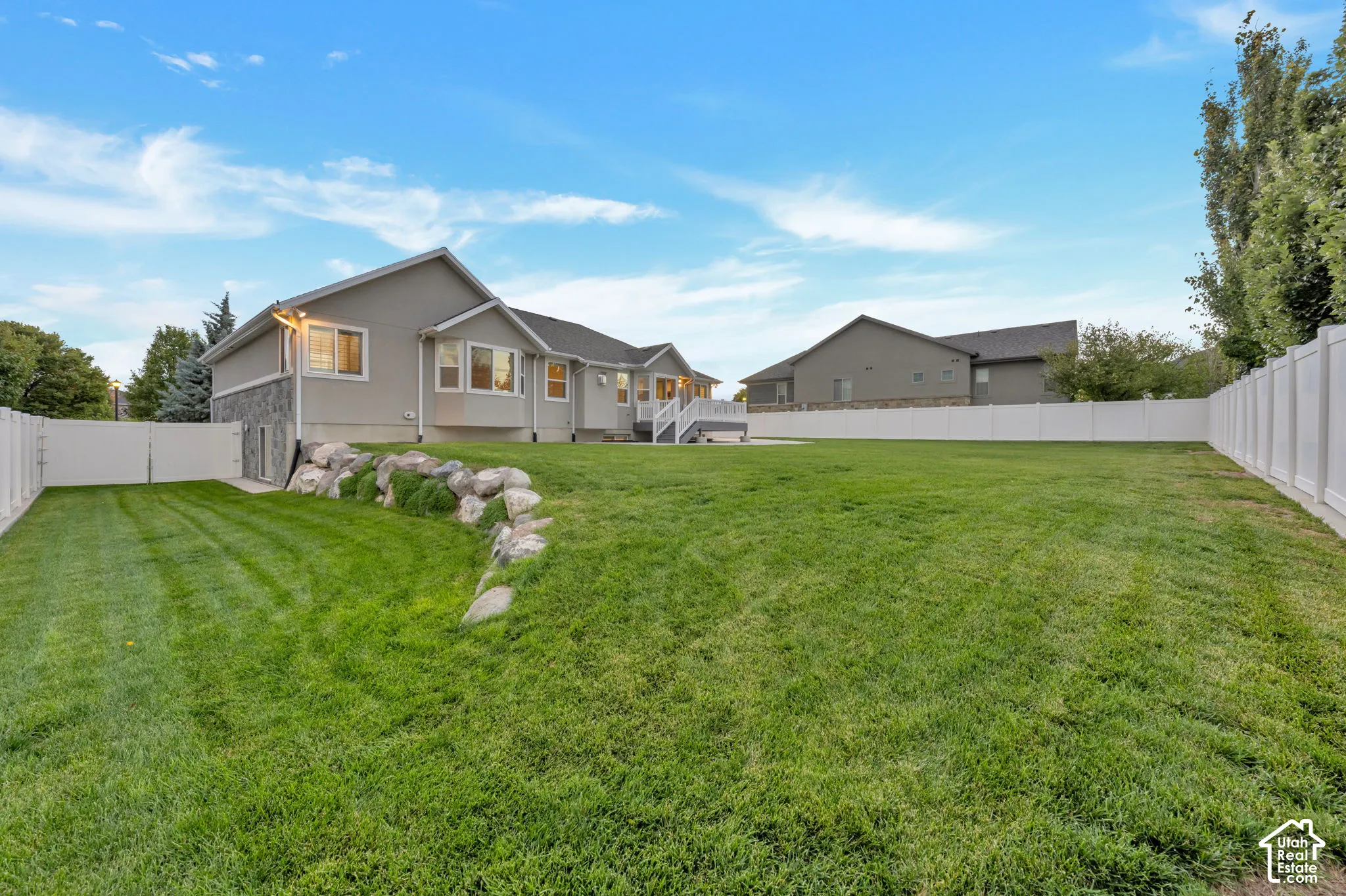 Expansive backyard featuring a tiered lawn, natural stone retaining wall, perimeter vinyl fencing, and an elevated composite deck